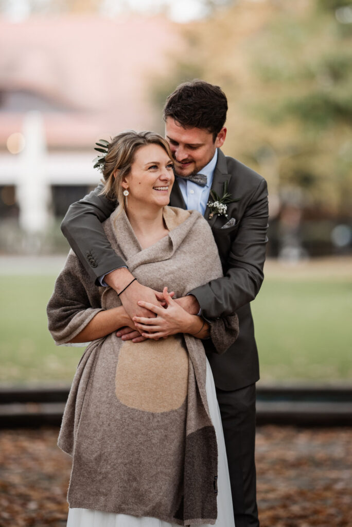 Bräutigam umarmt seine Braut vor dem Stadtparkcafé in Fürth. Das Hochzeitsfoto stammt von der Fotografin Kristina Reinartz