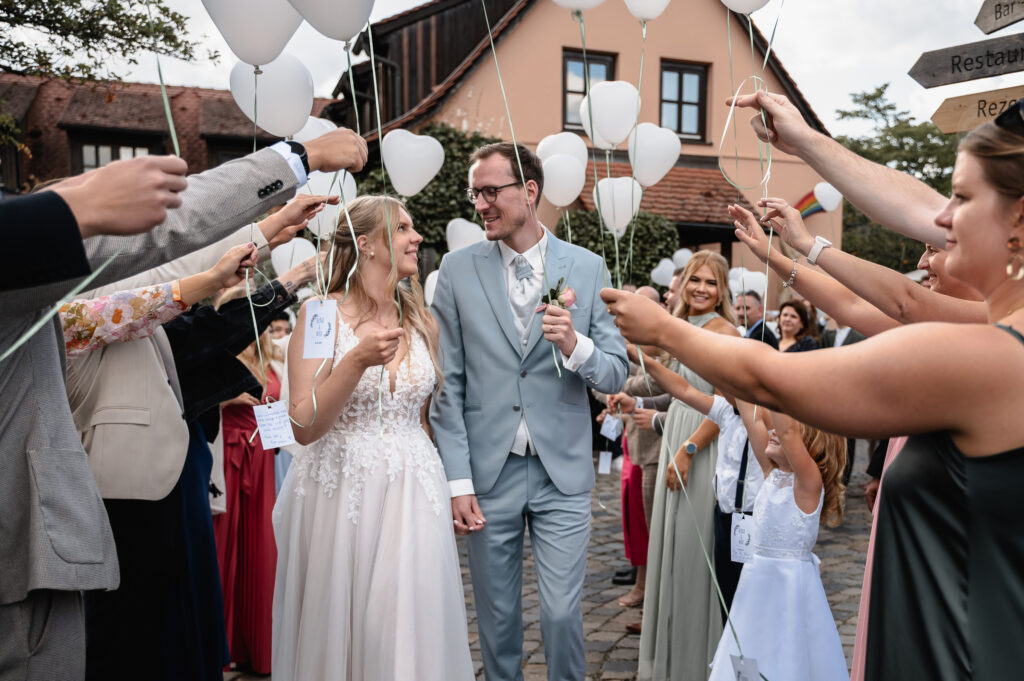 Brautpaar schreitet am Schindlerhof Nürnberg durch ein Spalier mit Luftballons. 